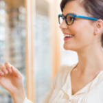 Happy young woman trying new glasses at optician store